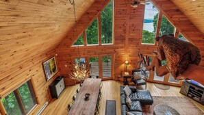 A log cabin interior with a dining area, seating, a fireplace, and large windows. - Escape to Summit View Lodge in Mountaintop, a spacious pet-friendly retreat for 14! (McHenry)