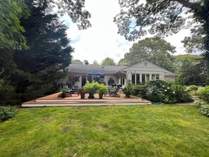 Ein Haus mit überdachter Terrasse, Rasen und umliegenden Bäumen.