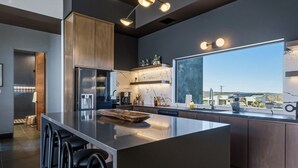 A modern kitchen with a large island, bar stools, a refrigerator, and a window with a view. - Skyhaven Luxe - Pool/Spa Pickleball Sauna (Joshua Tree)