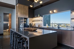 A modern kitchen with a large island, bar stools, a refrigerator, and a window with a view. - Skyhaven Luxe - Pool/Spa Pickleball Sauna (Joshua Tree)