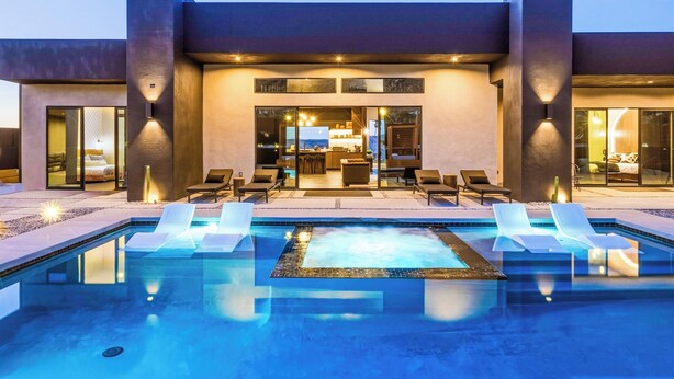 A modern building with a pool, lounge chairs, and a well-lit interior. - Skyhaven Luxe - Pool/Spa Pickleball Sauna (Joshua Tree)