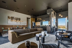 A modern living room with a sectional sofa, a coffee table, and a dining area with a table and chairs. - Skyhaven Luxe - Pool/Spa Pickleball Sauna (Joshua Tree)