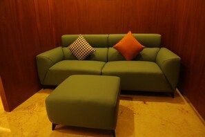 A green sofa with two pillows and a matching ottoman in a room with wooden paneling.