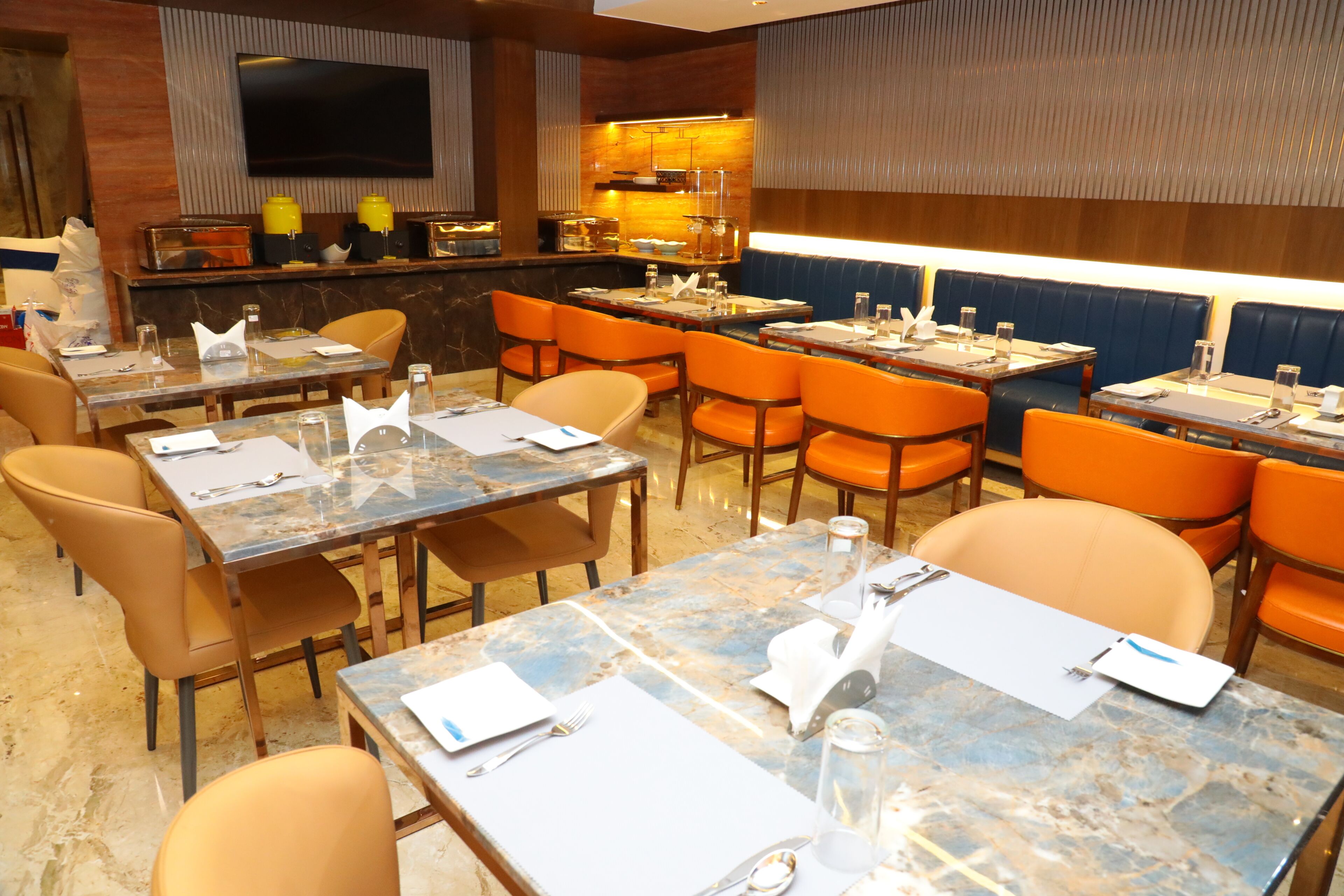 A restaurant with marble tables, orange chairs, and a bar area with a TV.