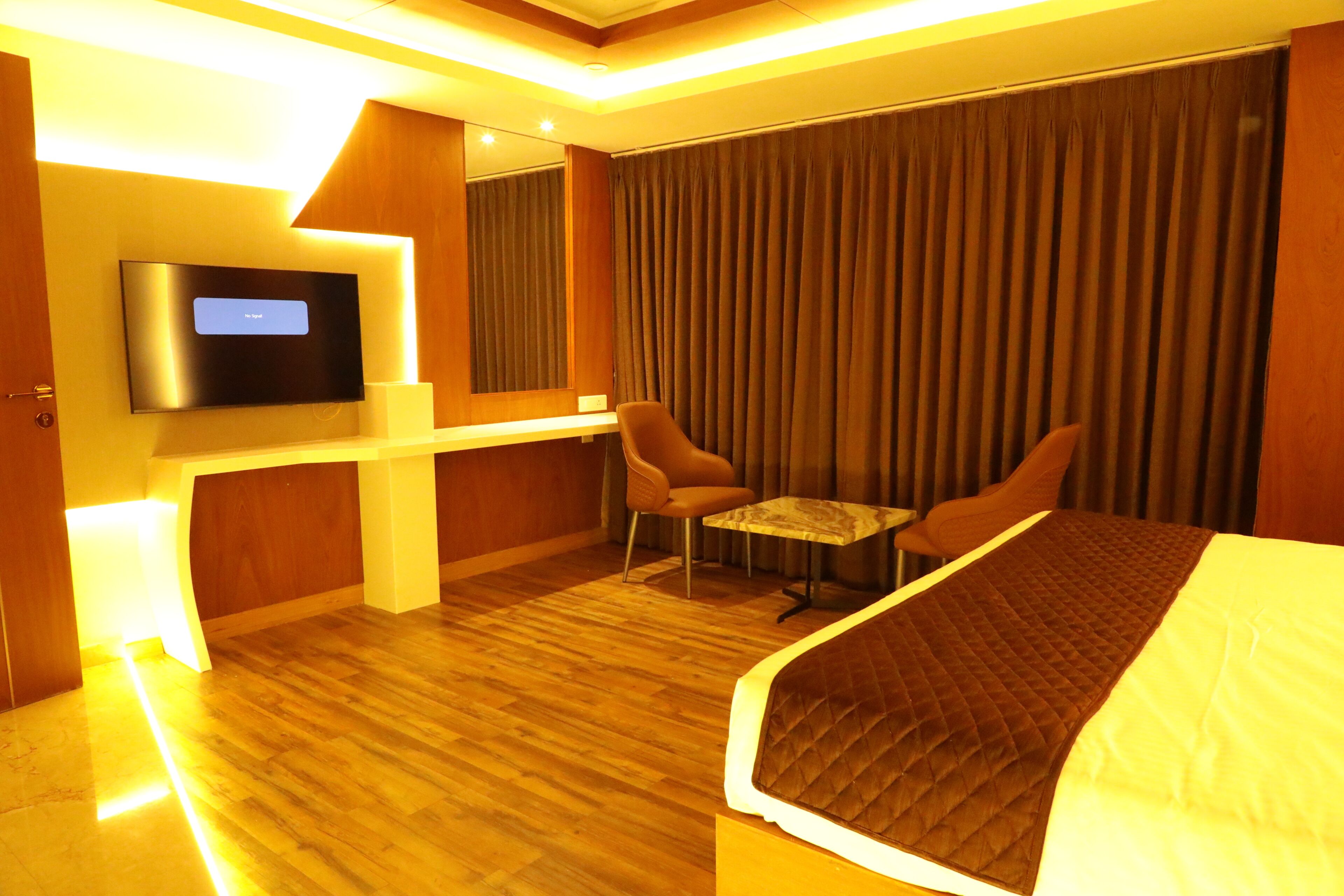 A hotel room with a bed, a TV mounted on the wall, a desk with a chair, and a window with curtains.