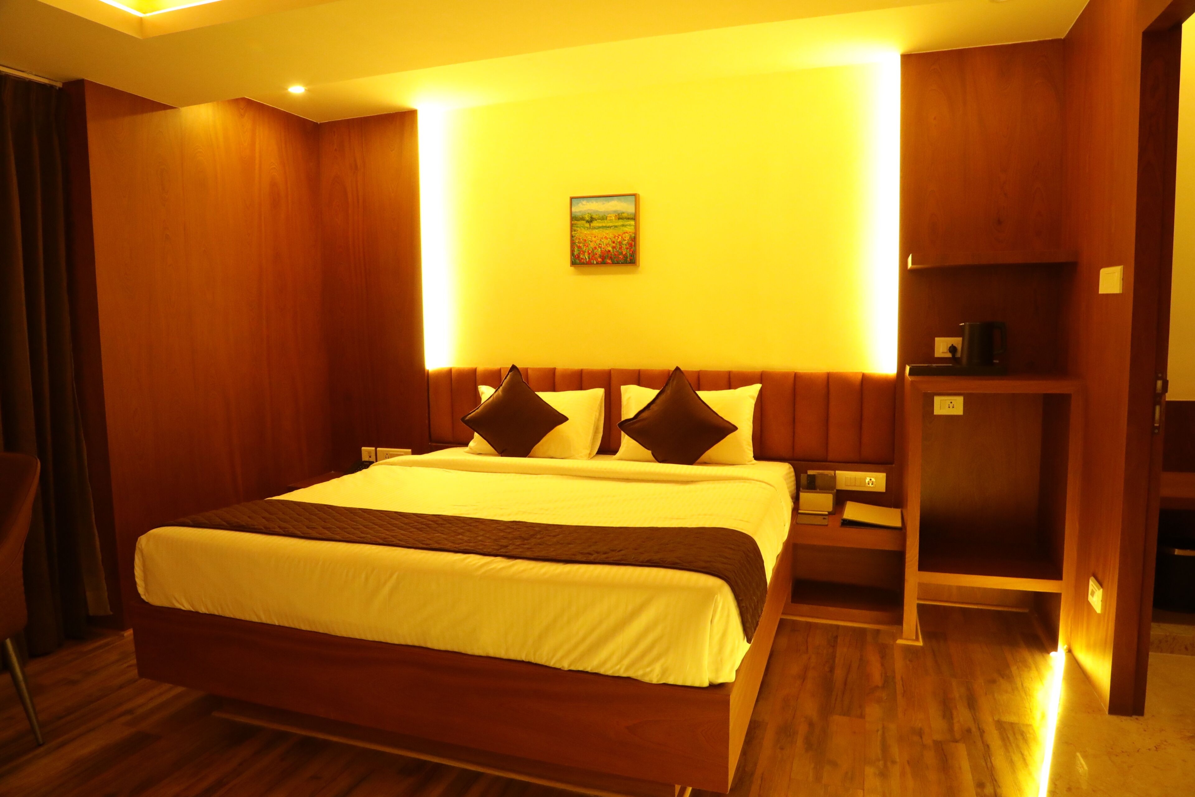 A hotel room with a large bed, wooden walls, a painting on the wall, and a nightstand with a lamp.