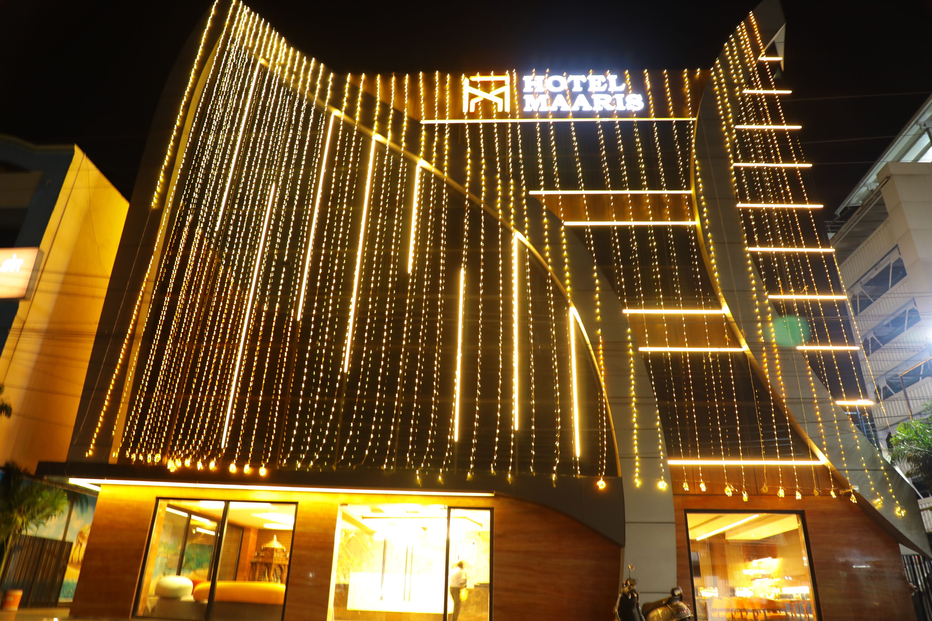 A hotel with a modern facade, illuminated string lights, and a prominent sign.