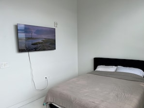 Ein Schlafzimmer mit einem Bett, einem an der Wand befestigten Fernseher, der eine Landschaft zeigt, und einer Steckdose.