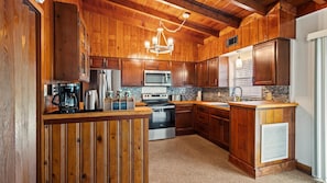 A kitchen with wooden cabinets, a stainless steel refrigerator, a microwave, a stove, and a coffee maker. - 2BR Coastal Cottage Near Downtown & Beaches (Vero Beach)