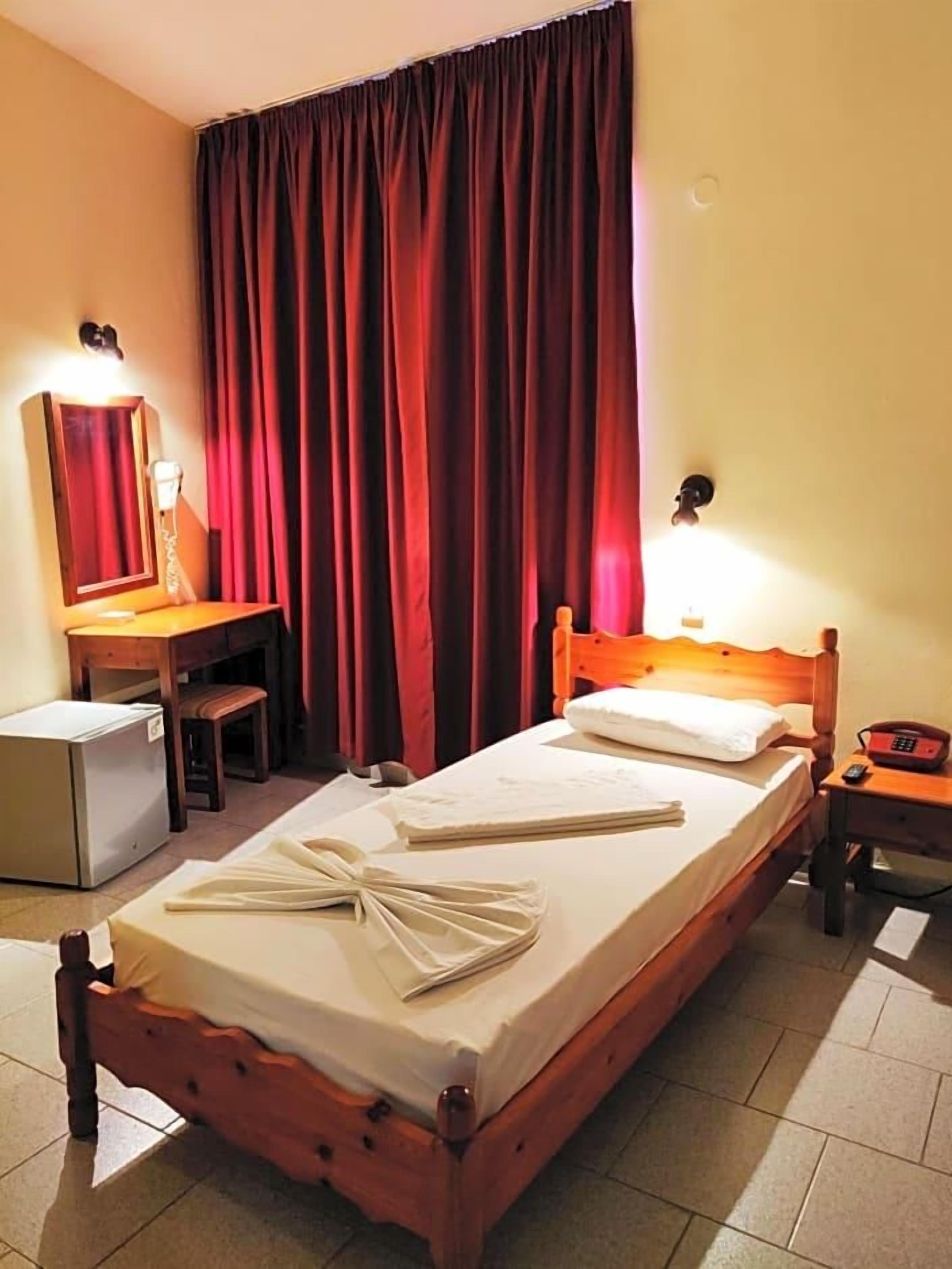 Ein Hotelzimmer mit Bett, Schreibtisch, Stuhl, kleinem Kühlschrank und Telefon.