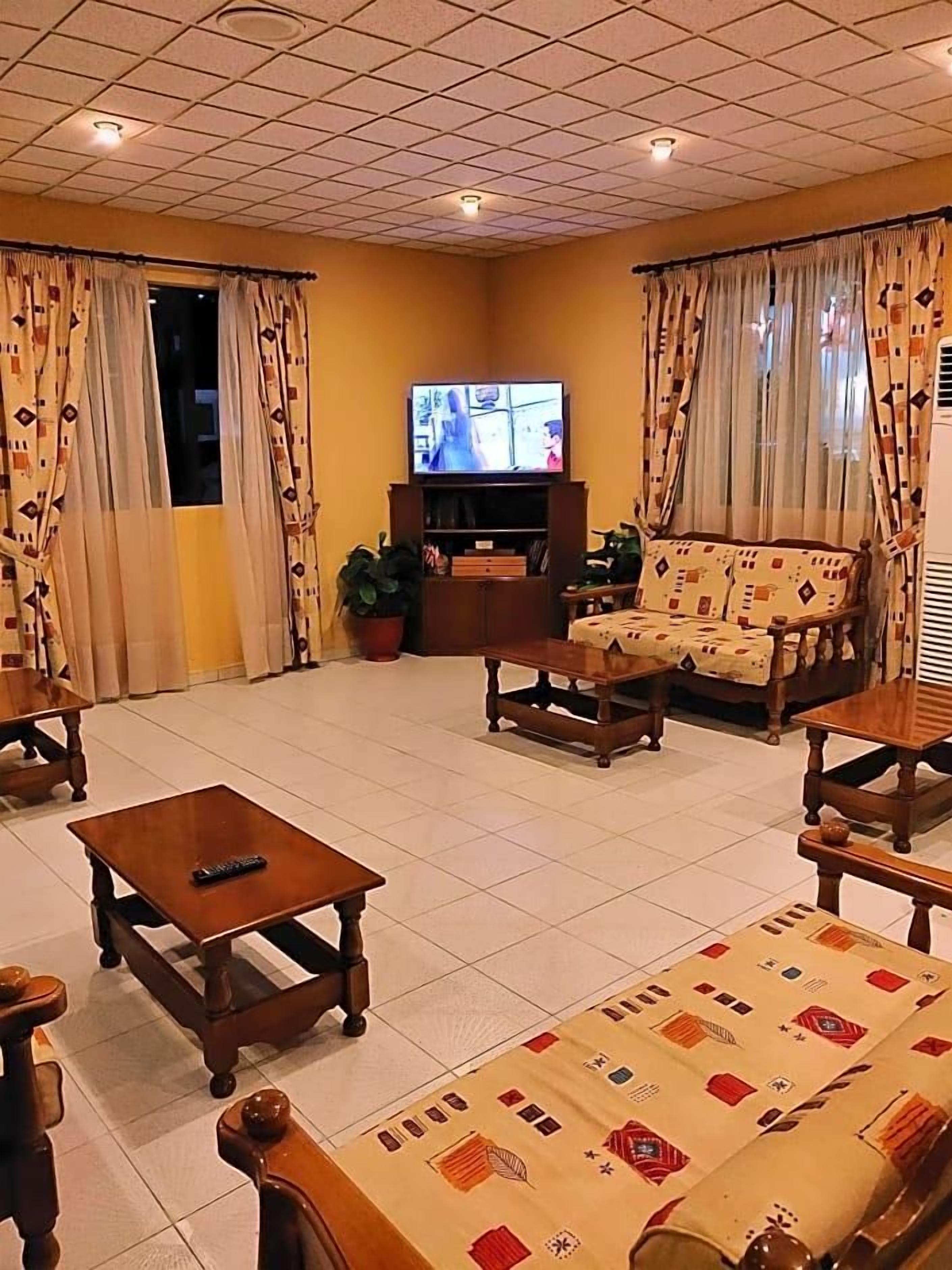 Ein Wohnzimmer mit Fernseher, Sofa, Sesseln, Couchtisch und Vorhängen.