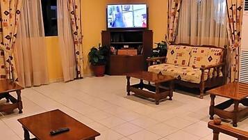 Ein Wohnzimmer mit Fernseher, Sofa, Sesseln, Couchtisch und Vorhängen.