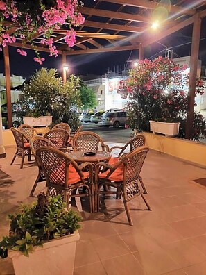 An outdoor seating area with wicker chairs and tables, surrounded by potted plants and flowers. - Titania - Karpathos (Karpathos)