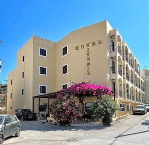 A hotel with a beige facade, multiple windows, and a covered entrance area with pink flowers. - Titania - Karpathos (Karpathos)