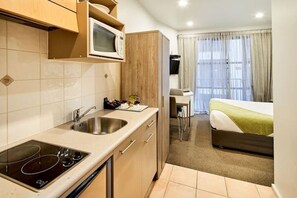 Een compacte hotelkamer met een kitchenette, een bed, een bureau en een raam met gordijnen.