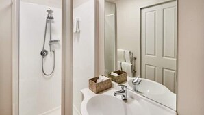 A bathroom with a white sink, a mirror, a shower, and two small wooden baskets.