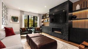 A modern living room with a fireplace, sofas, ottomans, and a TV. - VIEW from 2 Rooftop Decks, Walk to Kerry Park, Minutes to DT and Space Needle (Seattle)