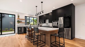 A modern kitchen with black cabinets, stainless steel appliances, and a central island with bar stools. - VIEW from 2 Rooftop Decks, Walk to Kerry Park, Minutes to DT and Space Needle (Seattle)