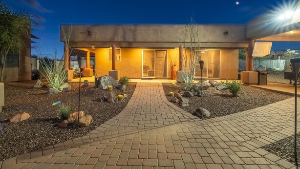 Una casa moderna con entrada iluminada, estacionamiento pavimentado y mobiliario exterior.