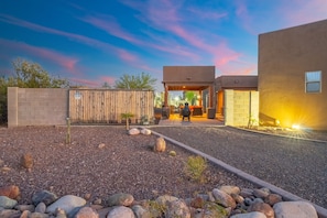 A modern building with a covered outdoor seating area, a gravel driveway, and a wooden fence.