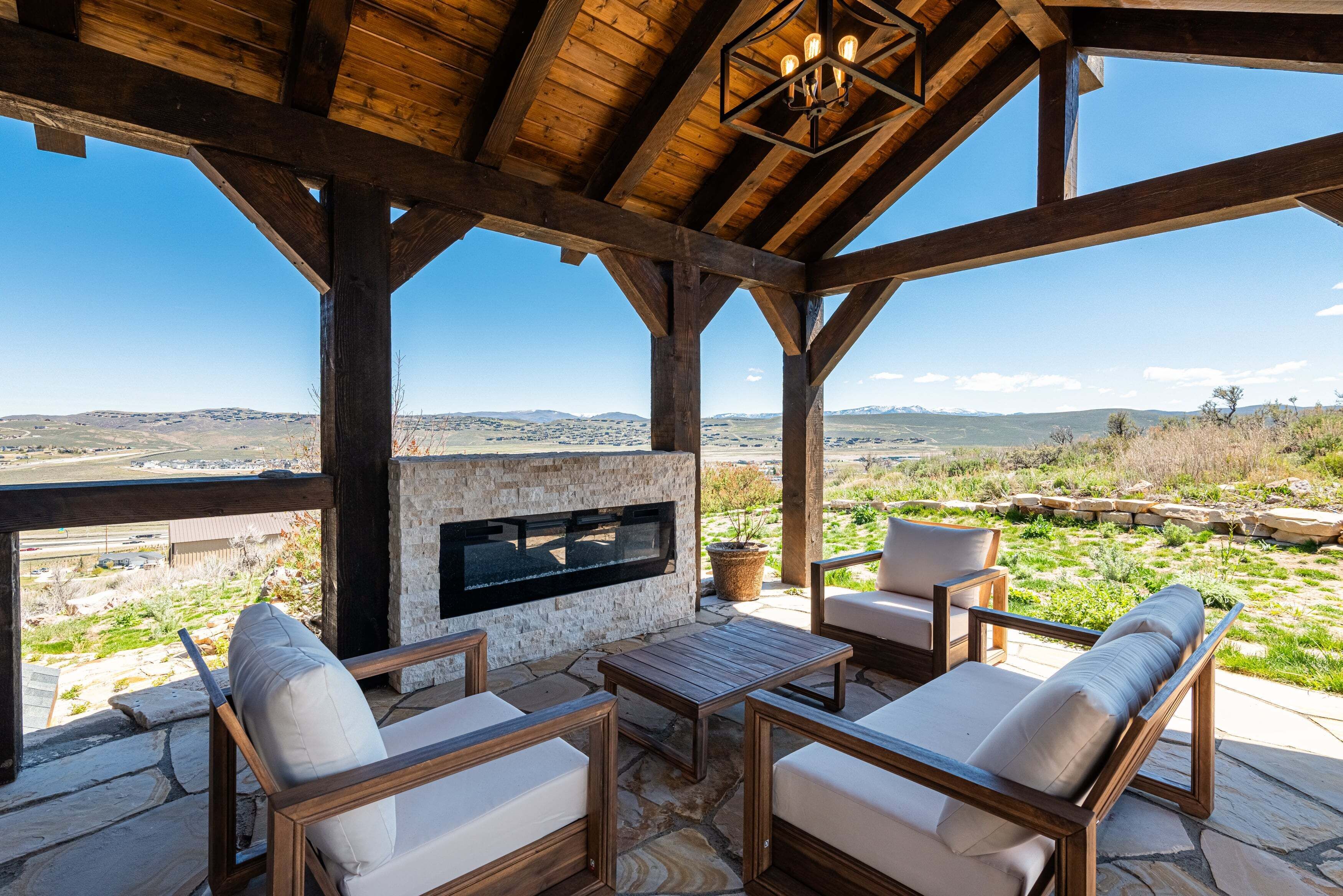 Un espace extérieur aménagé avec des sièges, protégé par un toit, doté d’un sol en pierre, de mobilier en bois et d’une cheminée en pierre.