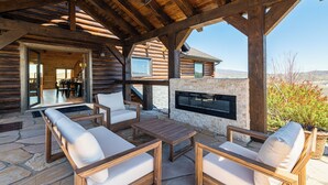 Eine Blockhütte mit einer Steinterrasse, Sitzgelegenheiten im Freien, einem Kamin und Blick auf die Landschaft.