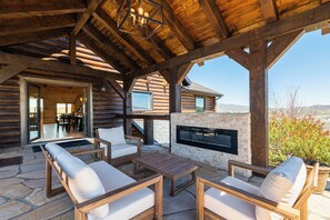 Eine Blockhütte mit einer Steinterrasse, Sitzgelegenheiten im Freien, einem Kamin und Blick auf die Landschaft.