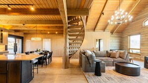 Ein Holzblockhaus-Interieur mit Wendeltreppe, Essbereich, Wohnzimmer mit Sofa und Küche mit großer Kochinsel.