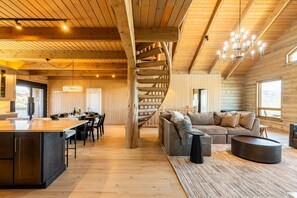 Ein Holzblockhaus-Interieur mit Wendeltreppe, Essbereich, Wohnzimmer mit Sofa und Küche mit großer Kochinsel.