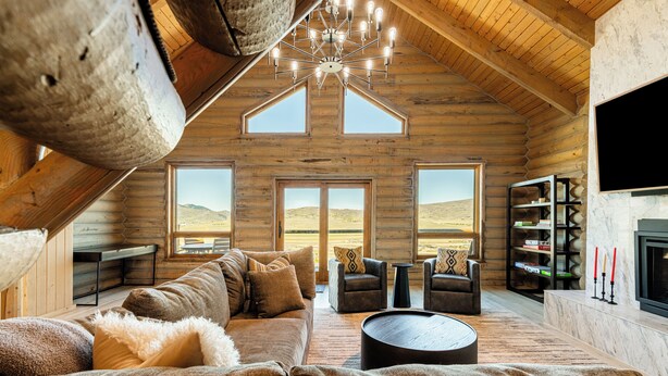 Ein gemütliches Blockhaus-Interieur mit einer großen Couch, zwei Sesseln, einem Couchtisch, einem Kamin und einem Bücherregal.