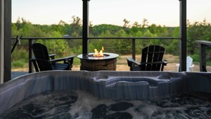 A hot tub with a fire pit, two chairs, and a view of a vineyard. - Hazel Hollow | Hot Tub w/ TV • Steam Shower • RRG (Rogers)