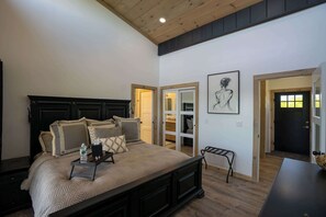 A bedroom with a large bed, a nightstand, a bench, and a door leading to a bathroom.