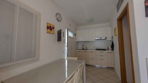 A compact kitchen with white cabinets, a dining table, and a clock on the wall. - Holiday apartment with balcony and air conditioning (Bibione)
