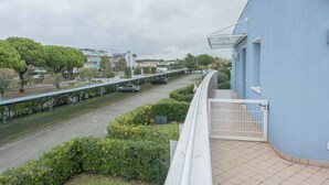 A residential building with a balcony, a paved road with cars, and greenery. - Holiday apartment with balcony and air conditioning (Bibione)