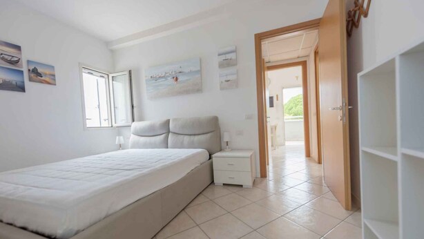 A bedroom with a bed, bedside table, and a door leading to another room. - Holiday apartment with balcony and air conditioning (Bibione)