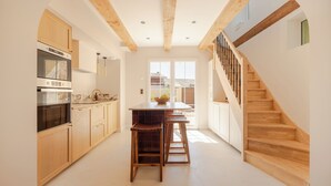 A modern kitchen with wooden beams, a central island, bar stools, and a staircase leading to an upper level. - Tour Vinea - Private Jacuzzi & 4K Cinema near Bordeaux (Villenave-d'Ornon)