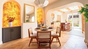 A dining area with a round table, chairs, and a vase of flowers. There is a kitchen in the background with wooden cabinets and a dining table. - Tour Vinea - Private Jacuzzi & 4K Cinema near Bordeaux (Villenave-d'Ornon)