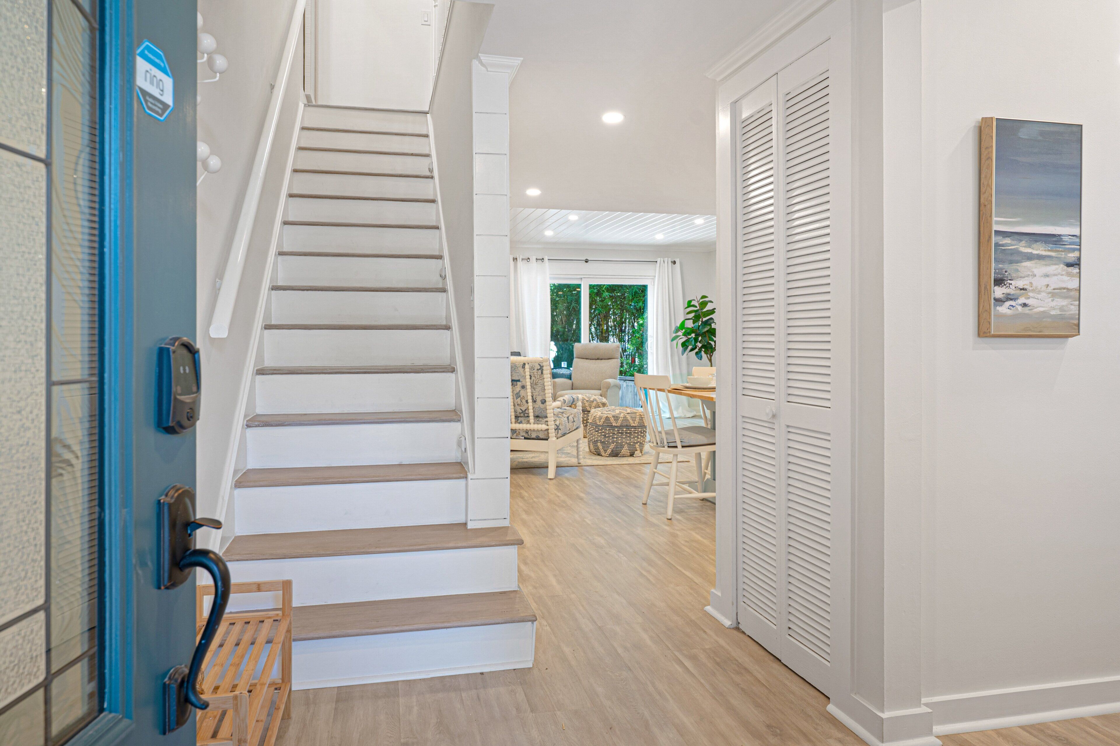 A staircase leading to a living area with a dining table and chairs, a potted plant, and a view of the outdoors.