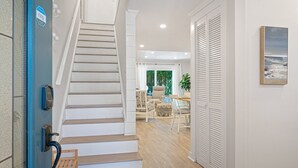 Una escalera conduce a una sala de estar con una mesa de comedor y sillas, una planta en maceta y vistas al exterior.
