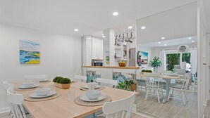 Una cocina moderna con muebles blancos, una mesa de comedor de madera y vistas al área de comedor contigua.