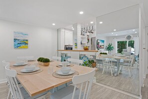 A modern kitchen with white cabinetry, a wooden dining table, and a view into the adjacent dining area. - Pet Friendly, Coastal Condo Near Folly Field Beach (Bluffton)