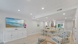 Un salón amplio con un televisor de pantalla plana grande, un comedor con mesa y sillas de madera, y una cocina al fondo.