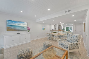 A spacious living room with a large flat-screen TV, a dining area with a wooden table and chairs, and a kitchen in the background. - Pet Friendly, Coastal Condo Near Folly Field Beach (Bluffton)