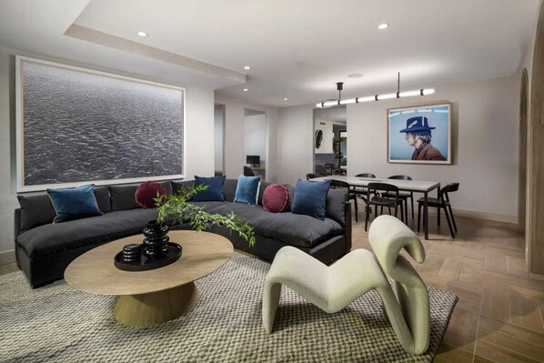 A modern living room with a sofa, coffee table, and chairs, a dining area with a table and chairs, and artwork on the walls.