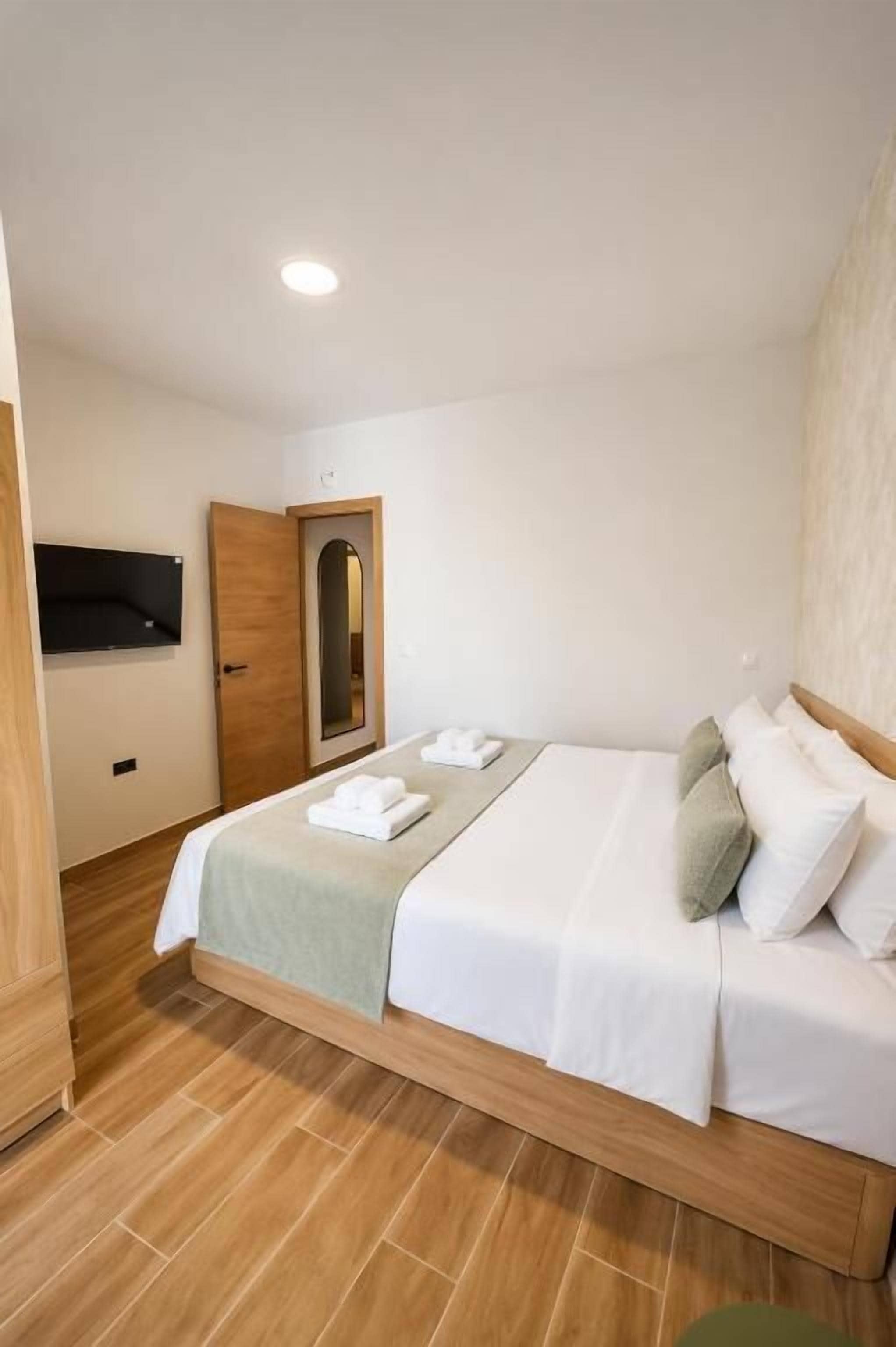 Una habitación de hotel con una cama, una puerta de madera, un espejo y un televisor de pantalla plana montado en la pared.
