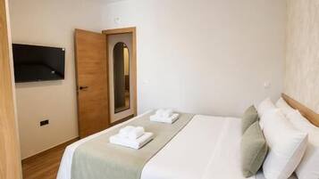 Una habitación de hotel con una cama, una puerta de madera, un espejo y un televisor de pantalla plana montado en la pared.