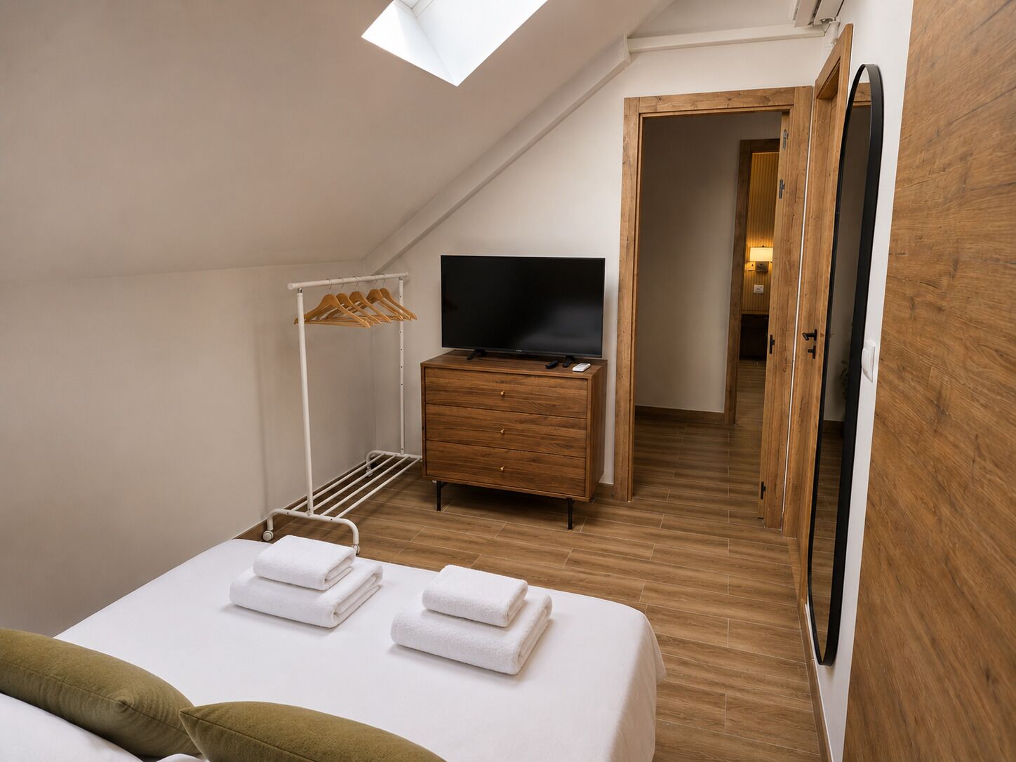 Un dormitorio con cama, televisión, cómoda de madera, vestidor y tragaluz.