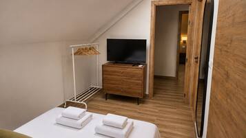 Un dormitorio con cama, televisión, cómoda de madera, vestidor y tragaluz.