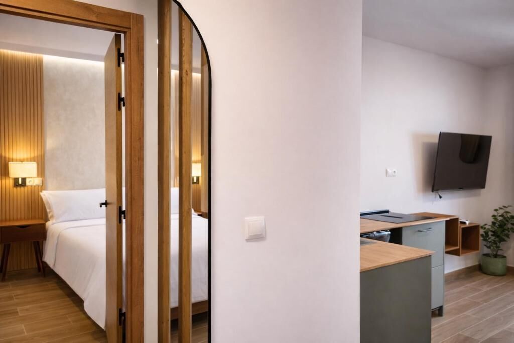 Una habitación de hotel moderna con cama, mesita de noche, lámpara y una pequeña kitchenette.