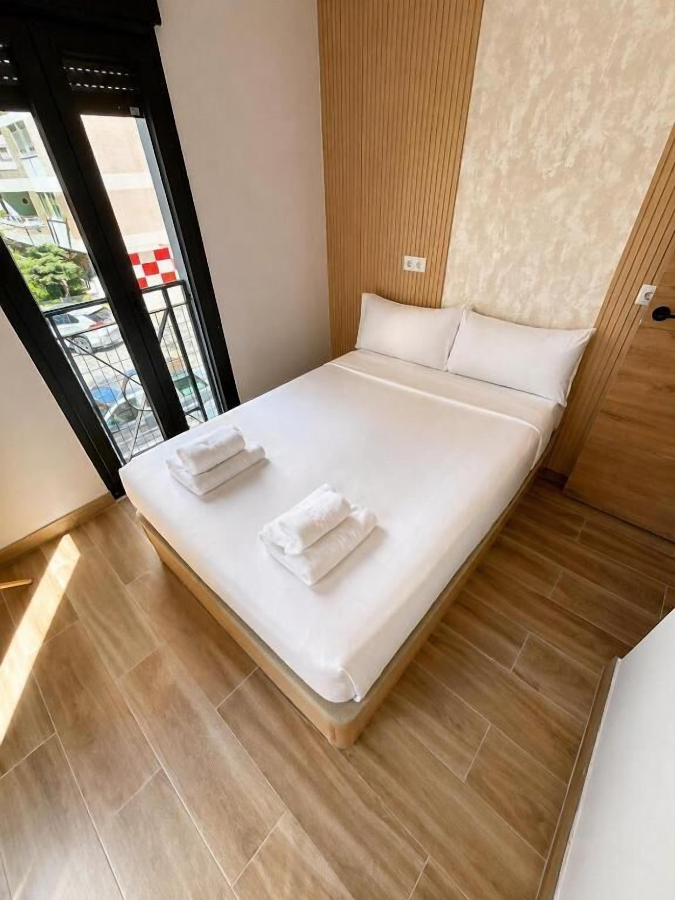 Une chambre d’hôtel avec un lit, un mur recouvert de panneaux en bois et une vue sur l’extérieur, visible à travers une porte.